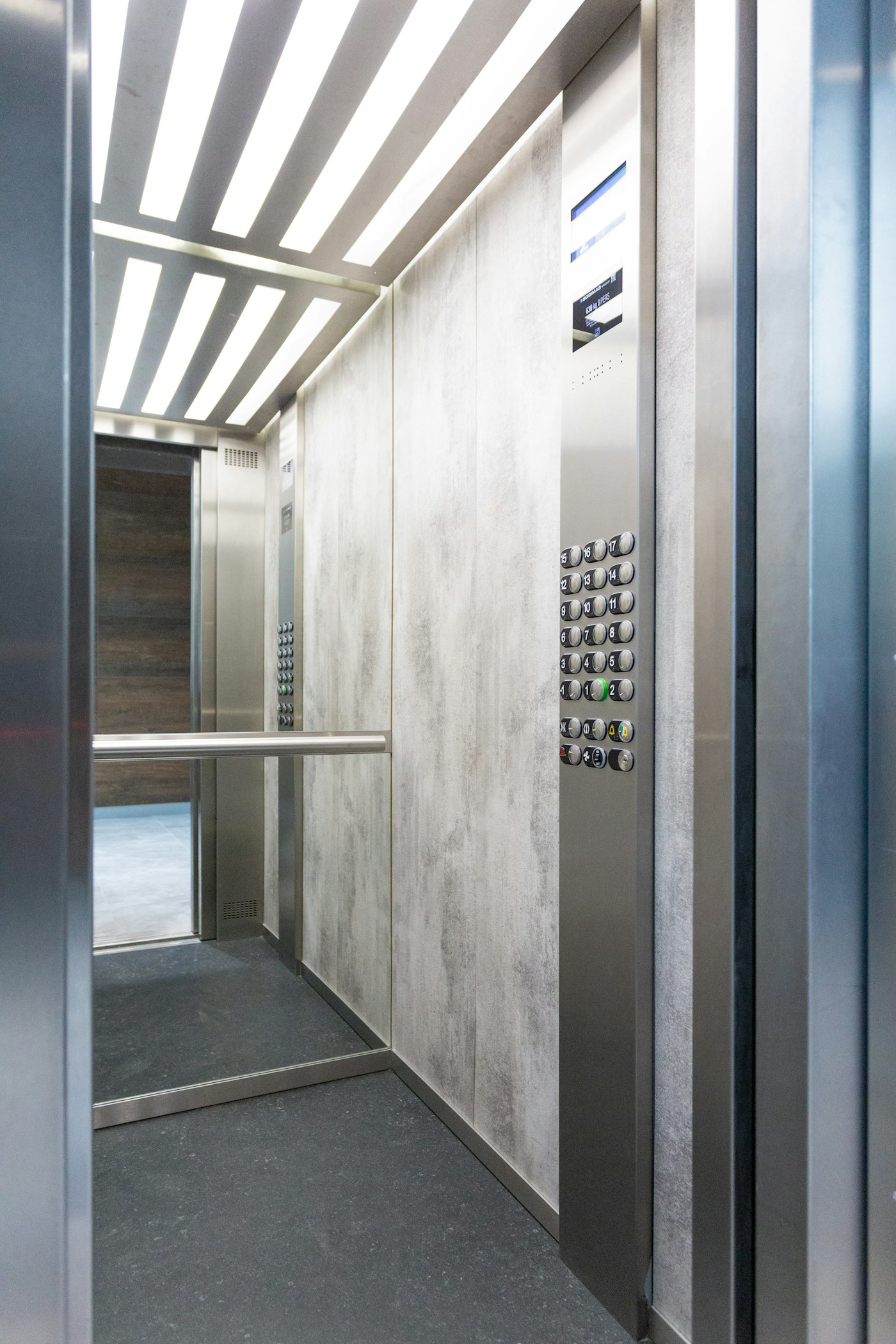 Cabina de elevador brillante con paneles de pared pálida, espejo, pasamanos y controles de acero inoxidable